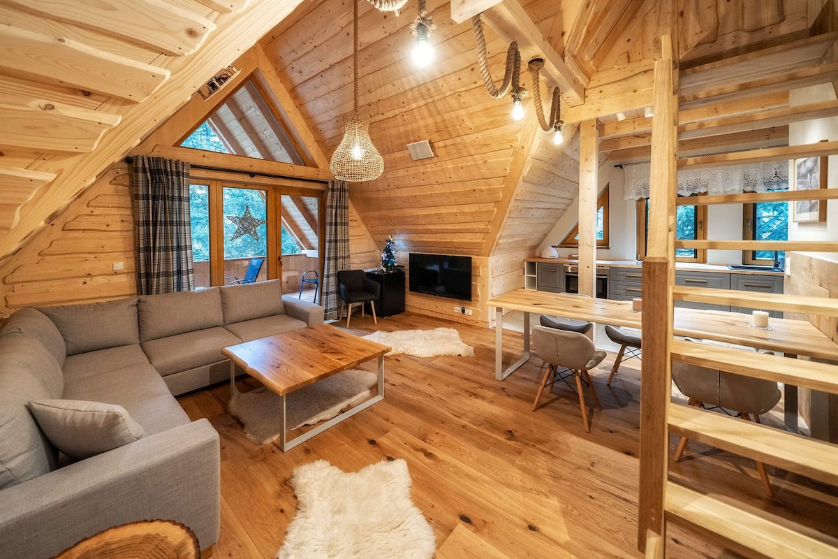 Un acogedor loft con techo de madera, un sofá gris, una mesa de comedor de madera y un televisor.