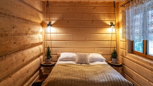 A cozy wooden cabin bedroom with a bed, two nightstands, a hanging plant, and a window with lace curtains. - Zakopiana (Zakopane)