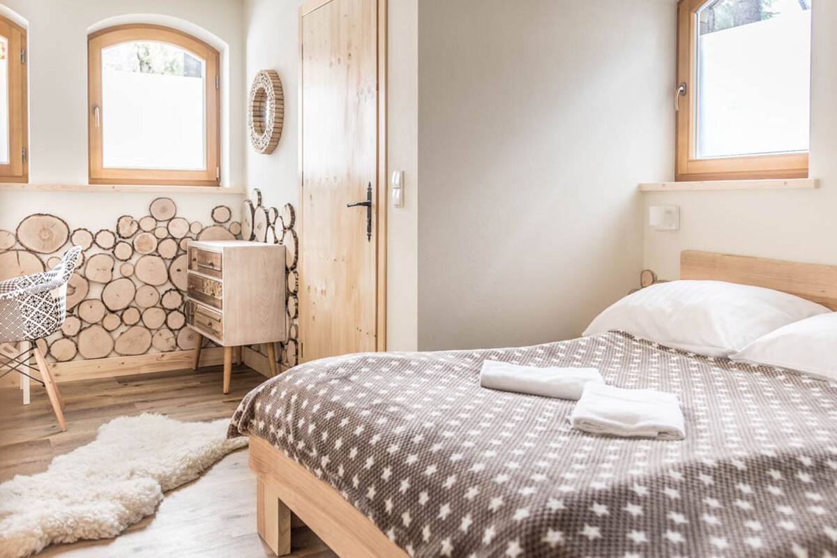 Un dormitorio con cama, cómoda de madera, una silla y una pared decorada con troncos.