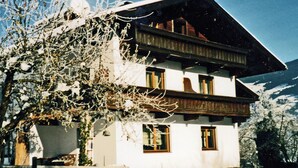 Una chaleta de dos pisos con techo inclinado, fachada de madera y varias ventanas.