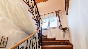 Una escalera de madera con barandillas de metal negro y un ventanal con cortinas de encaje.