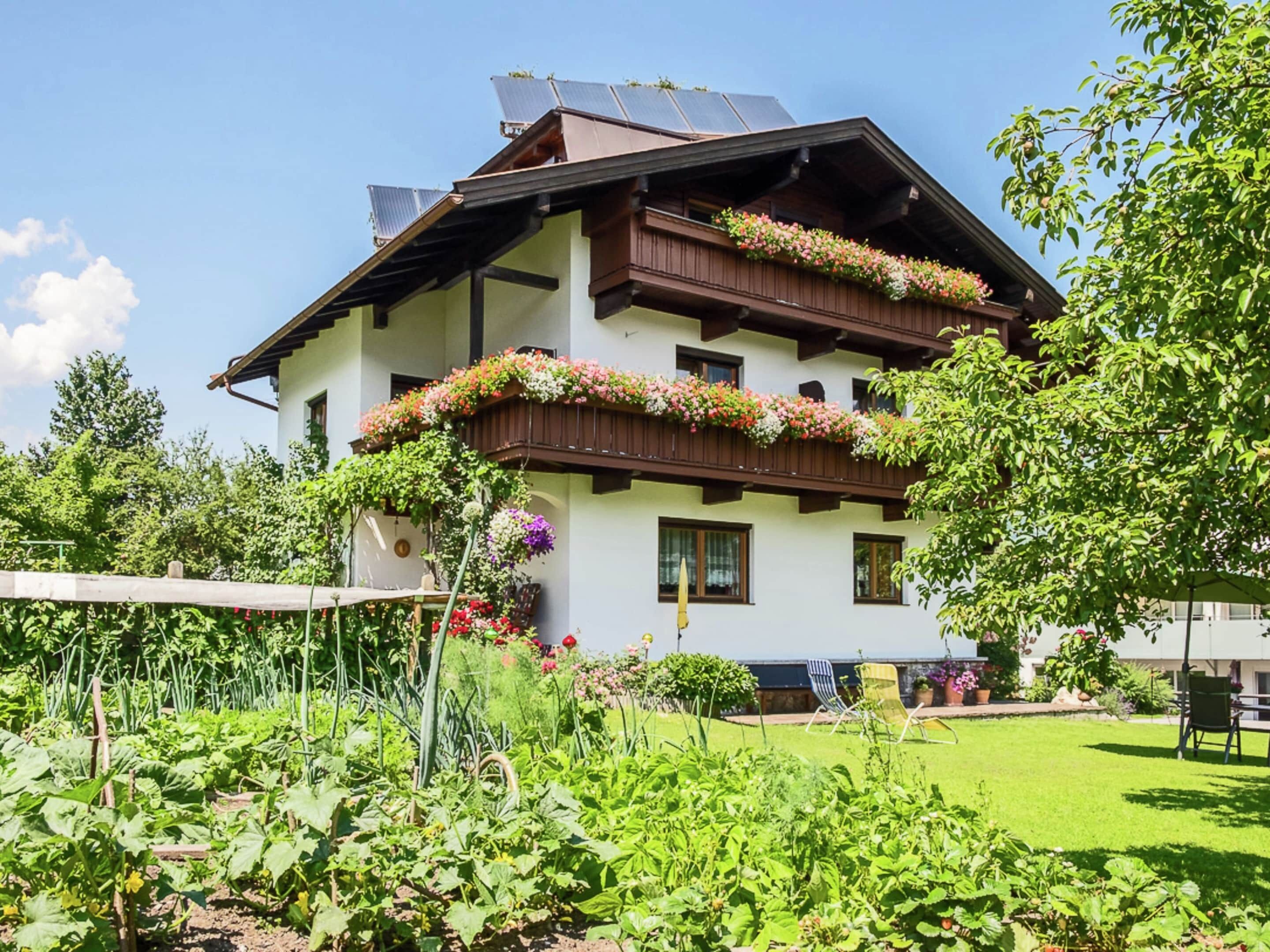 A multi-story building with balconies adorned with flowers, surrounded by a well-maintained garden.