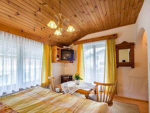 Una habitación acogedora con techo de madera, una cama, una mesa con sillas, un televisor y un espejo.