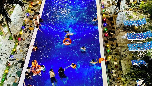 A swimming pool with people, surrounded by stone tiles and potted plants. - Elizabeth Hotel Tam Coc (Nam Hoa Lu)