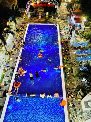 Piscina con gente, rodeada de baldosas de piedra y plantas en macetas.