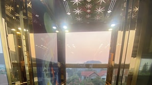 An elevator with a glass door, a patterned floor, and a view of pink flowers and buildings outside. - Elizabeth Hotel Tam Coc (Nam Hoa Lu)