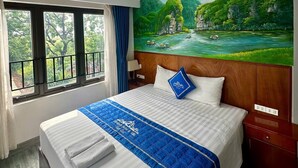 Une chambre d’hôtel avec un lit, un tableau représentant un paysage, une fenêtre donnant sur un beau panorama et une table de chevet.