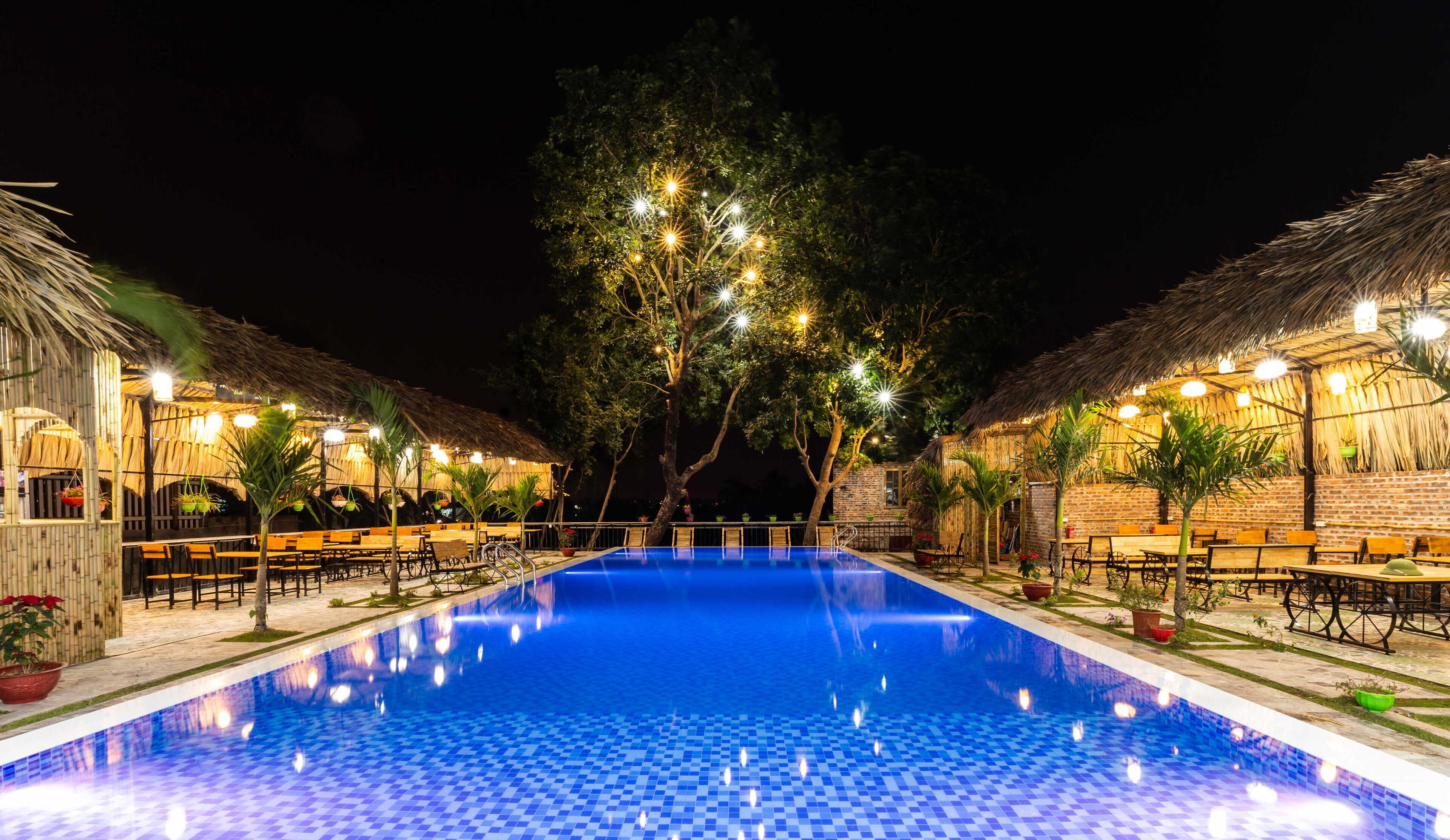 A nighttime swimming pool area with thatched-roof structures and outdoor seating.
