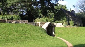 A stone building with a sloped roof, surrounded by a grassy area and trees. - Country house Quevarec (Dinéault)