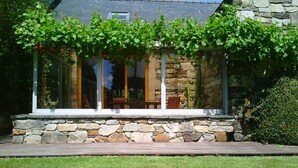 A stone house with a covered patio and a view of the interior through large windows. - Country house Quevarec (Dinéault)