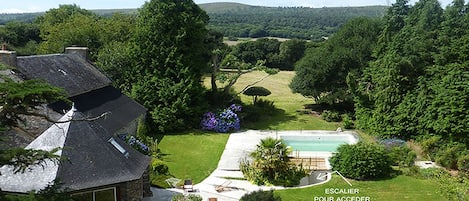 A house with a swimming pool, a staircase leading to the pool, and a view of the surrounding landscape.