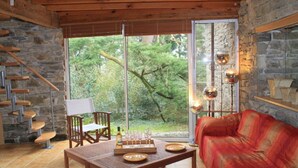A cozy room with a stone wall, wooden staircase, a red sofa, a wooden table with a chessboard, and a large window with a view of trees. - Country house Quevarec (Dinéault)