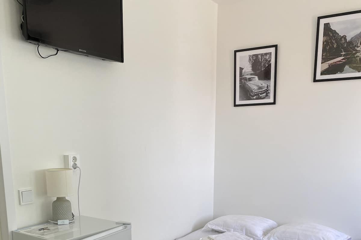 A small, clean room with a bed, a desk, a television, and two framed pictures on the wall.