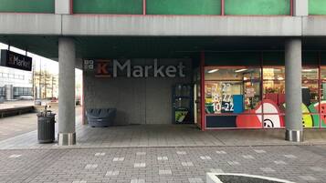 Una tienda K Market con fachada moderna, ventanas grandes y un bote de basura a la vista afuera.