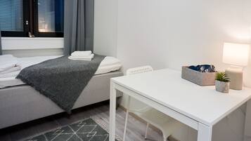 Un dormitorio ordenado con cama, mesita de noche, lámpara y una planta pequeña.