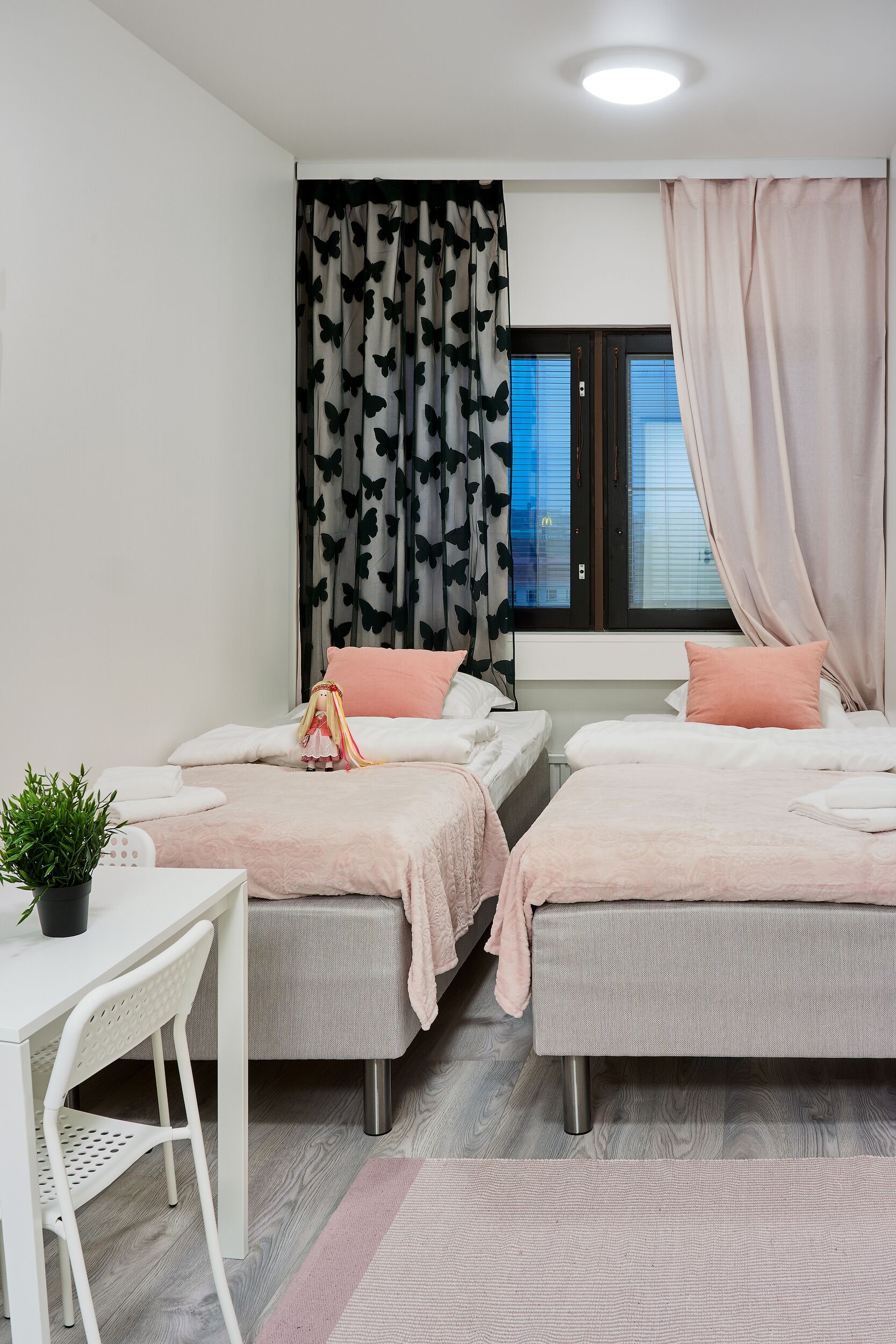 A bedroom with two beds, a desk, and a potted plant.