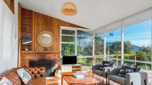 A modern living room with a fireplace, wooden shelves, a large window with a view of the outdoors, and a cozy seating area.