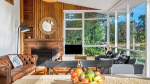 A living room with a fireplace, a television, and a large window offering a view of greenery.