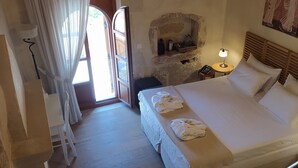 A hotel room with a bed, a chair, a nightstand, a lamp, a wall-mounted air conditioner, and a stone wall with a shelf. - Villa with garden, inneryard and terrace with a view to Talean Mountains (Melidoni Rethymni)