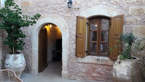 A stone building with an arched doorway, a window with wooden shutters, and potted plants. - Villa with garden, inneryard and terrace with a view to Talean Mountains (Melidoni Rethymni)