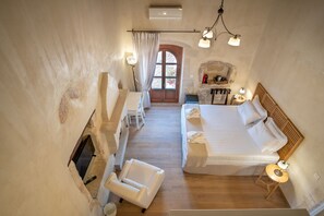 Une chambre avec un plancher en bois, un lit, une chaise, une petite table, une cheminée et une fenêtre avec des rideaux.
