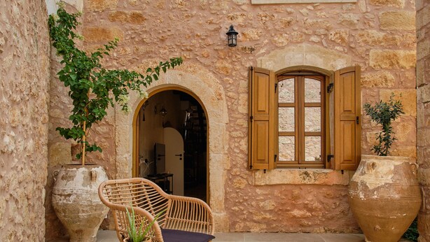 A courtyard with stone walls, two wooden-framed windows, wicker chairs, and potted plants. - Villa with garden, inneryard and terrace with a view to Talean Mountains (Melidoni Rethymni)