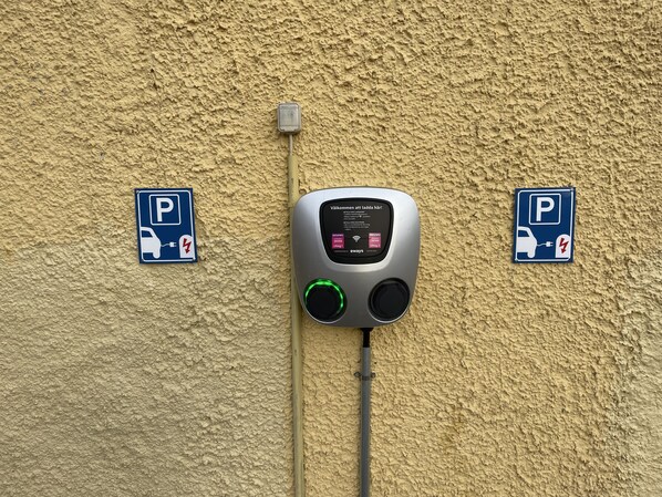 A wall-mounted electric vehicle charging station with two parking signs.