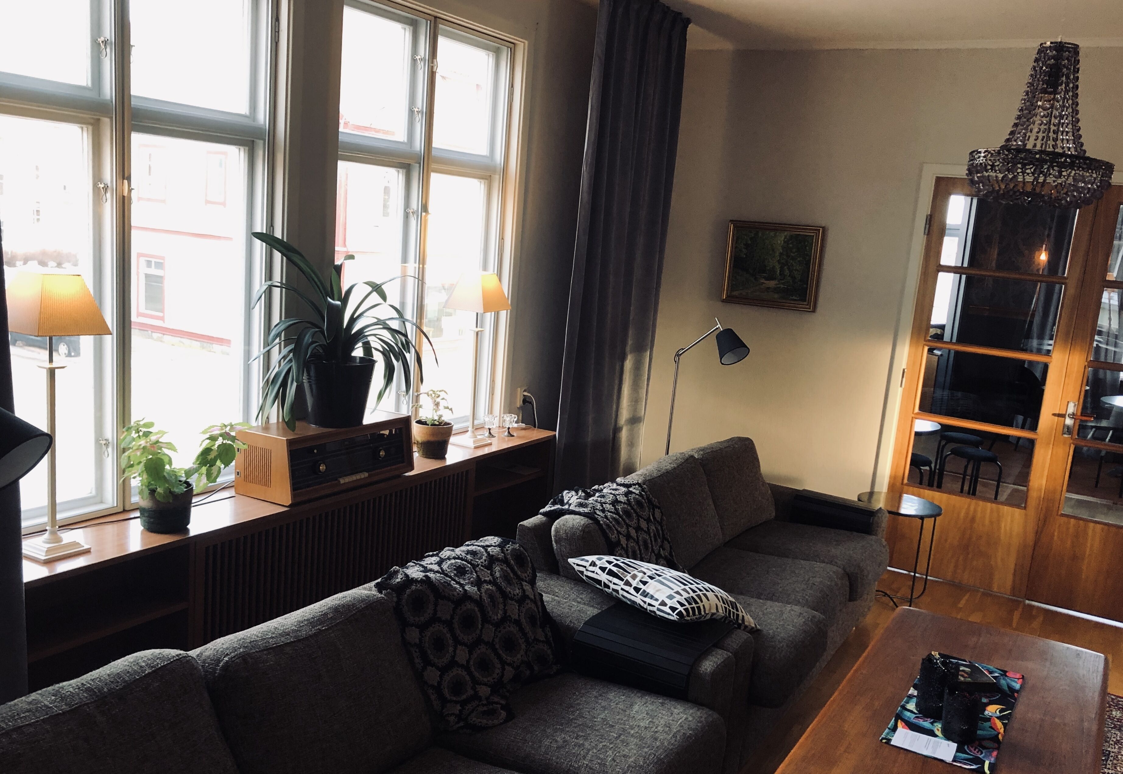 En stue med sofa, sofabord, bogreol, lampe og en plante.