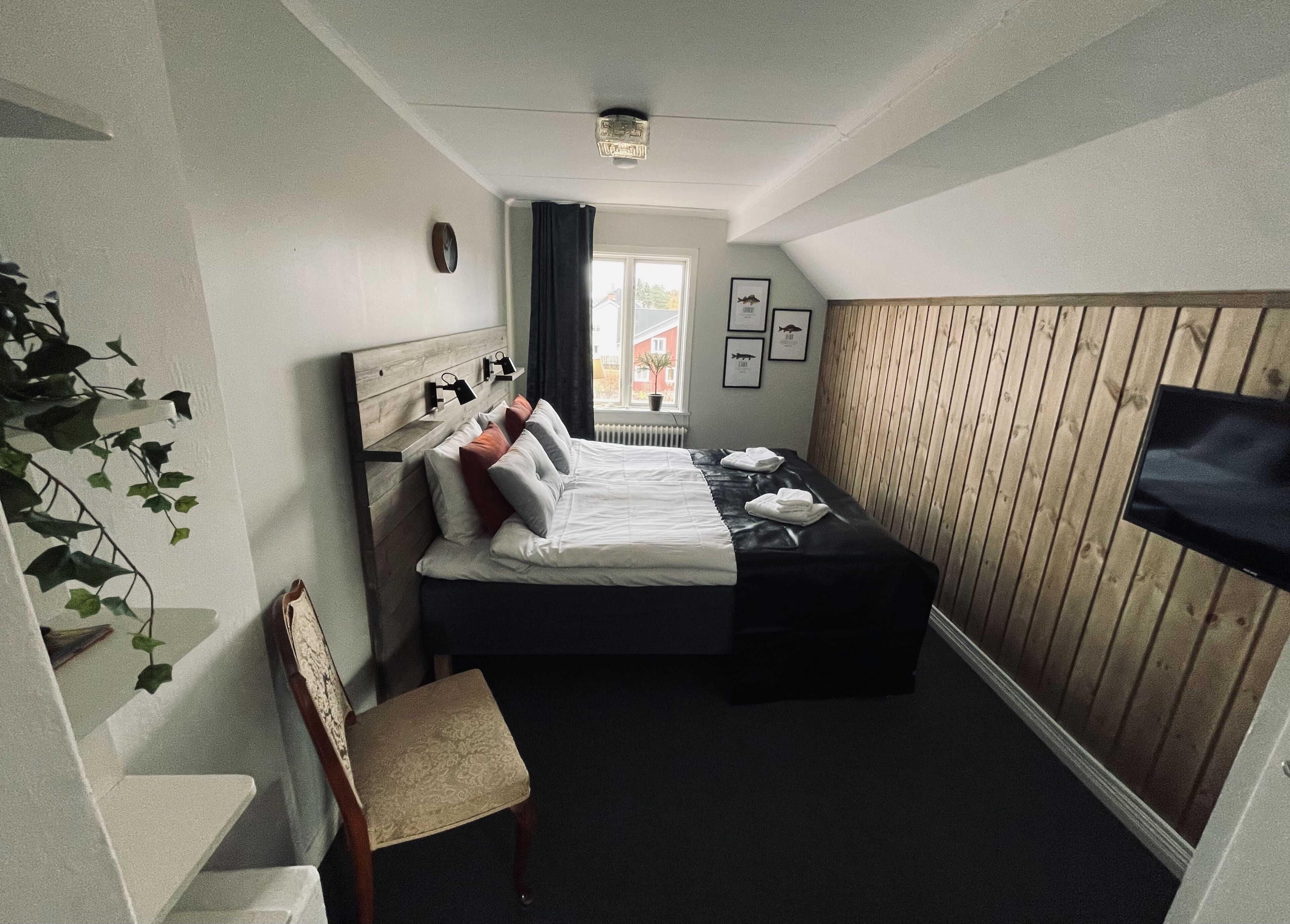 Una habitación de hotel compacta con cama, mesita de noche, silla y televisor en la pared.