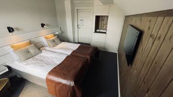 A hotel room with a bed, bedside tables, a TV mounted on the wall, and a wooden panel on one side.