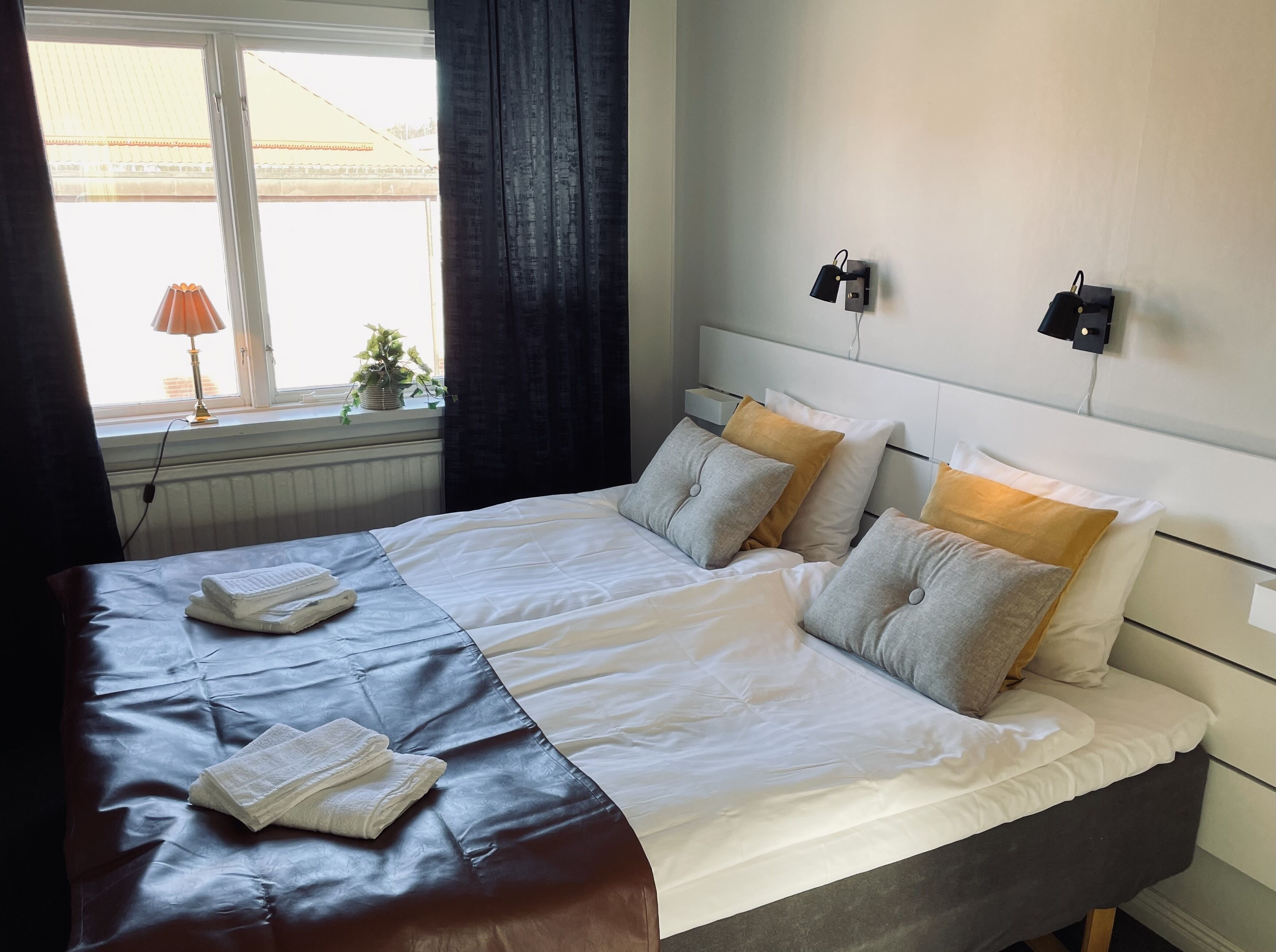 A neatly made bed with pillows and a blanket, a bedside lamp, and a window with curtains.