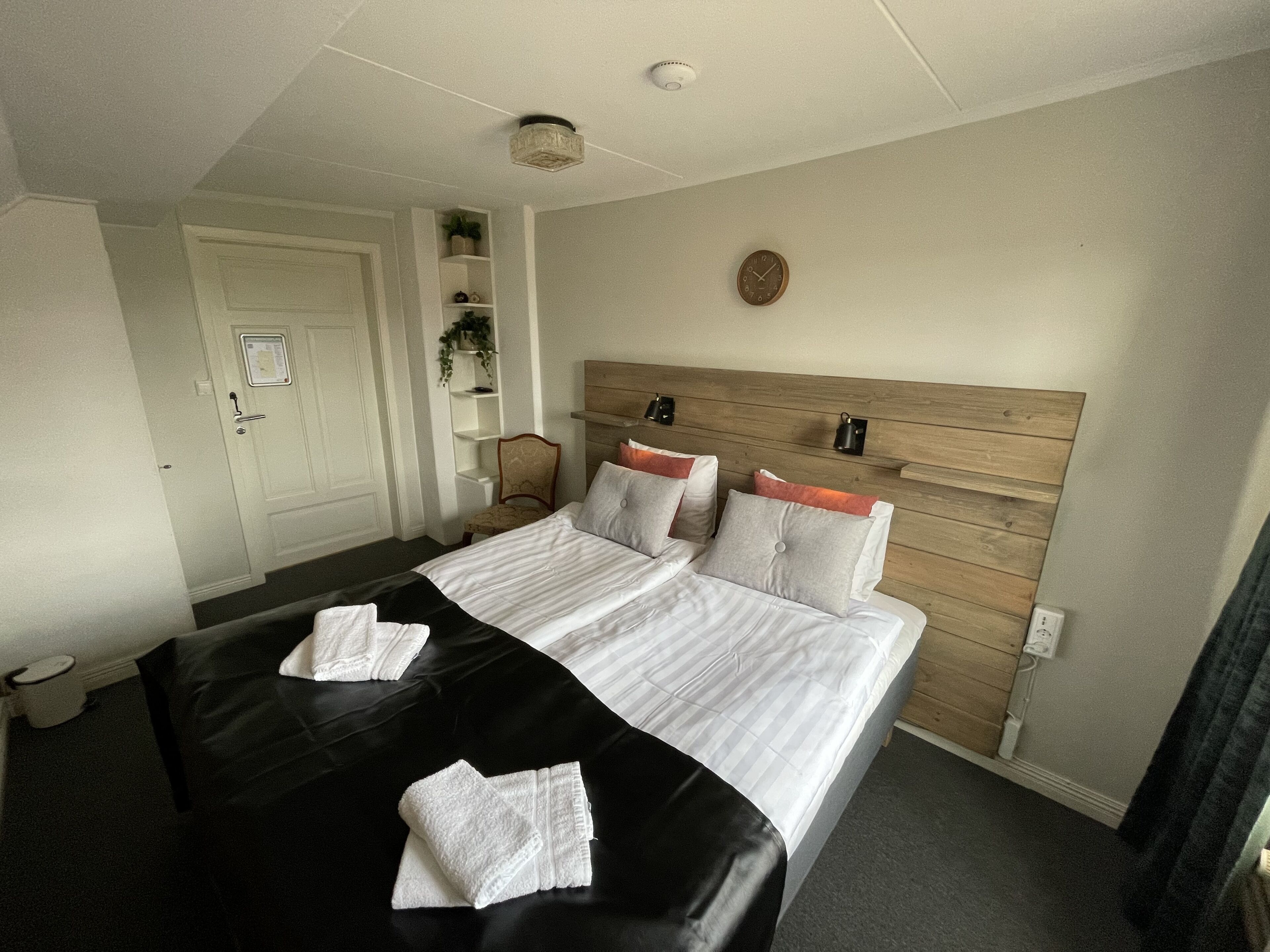 Una habitación de hotel con una cama grande, un cabecero de madera, una mesita de noche y un pequeño estante con una planta.