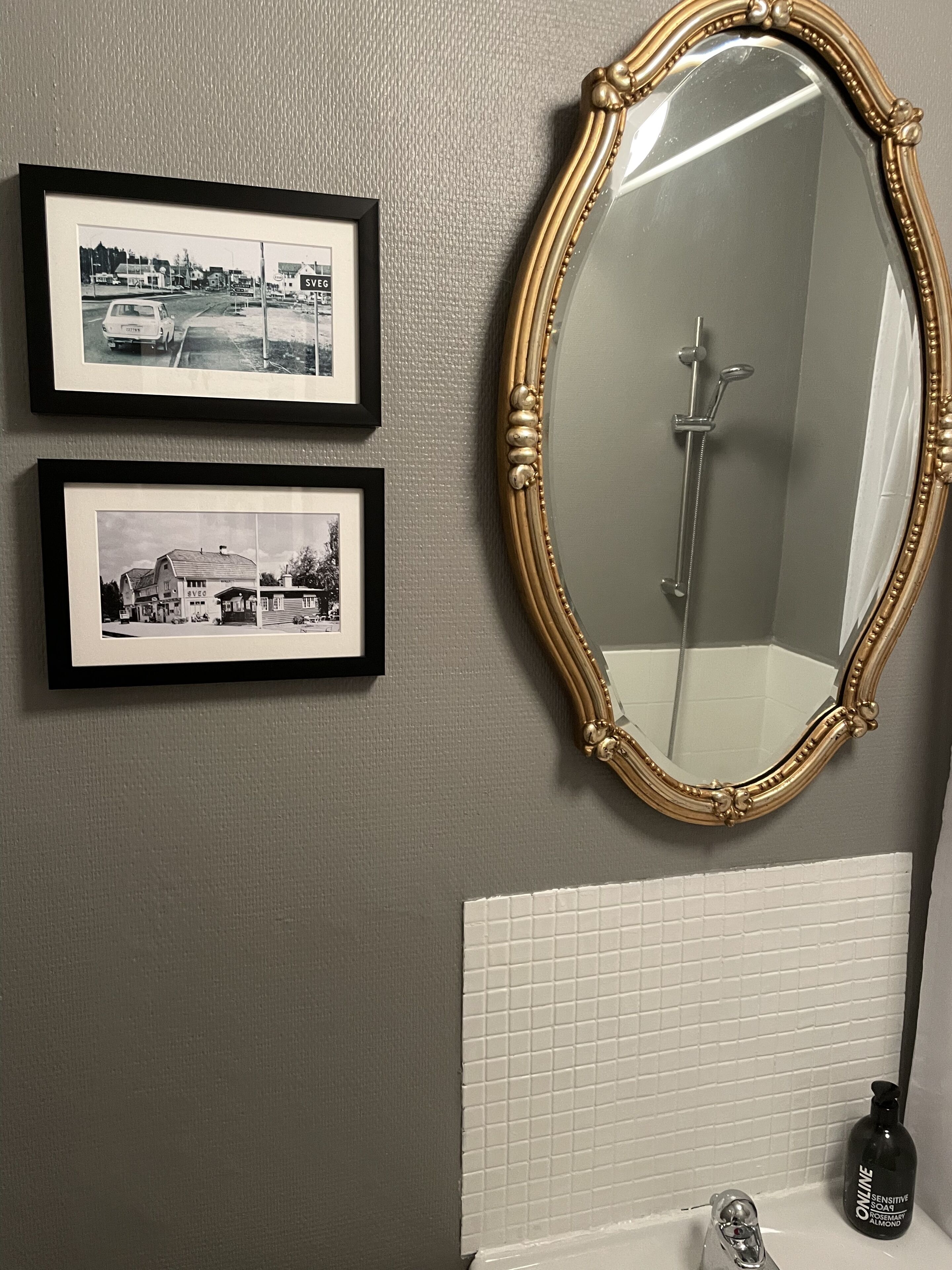 Een badkamer met een grote spiegel, twee ingelijste zwart-witfoto's en een zeepfles.