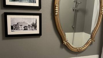 Une salle de bain avec un grand miroir, deux photos en noir et blanc encadrées et un flacon de savon.