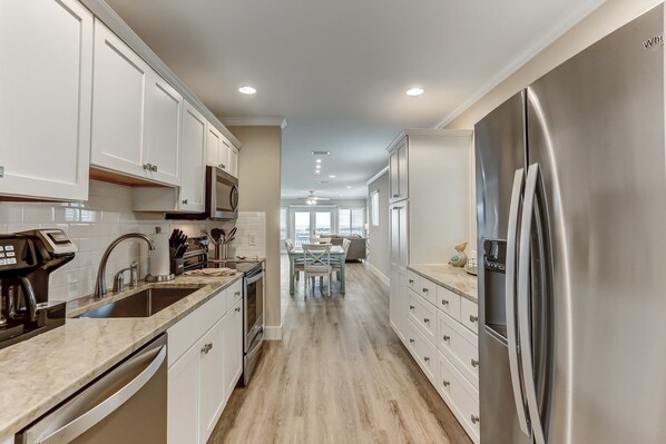 A modern kitchen with white cabinets, stainless steel appliances, and a wooden floor.