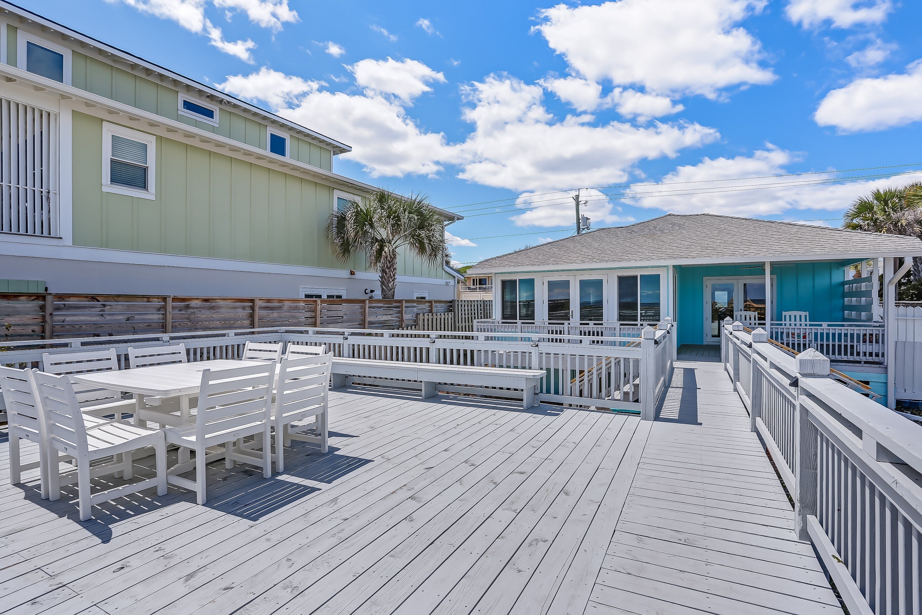 A wooden deck with white furniture and a view of a house with a blue roof.