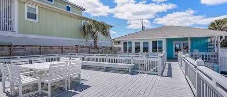 A wooden deck with white furniture and a view of a house with a blue roof.