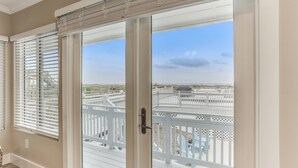 A room with a sliding glass door leading to a balcony with a white railing and a view of a white fence and a blue chair. - Oceanfront Beach House with Spacious Backyard by RedAwning (Fernandina Beach)