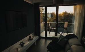 Relax in this stylish living room with a large flat-screen TV and sliding glass door leading to a balcony with outdoor seating.