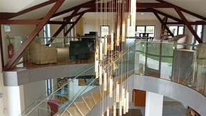 A spacious interior with a modern staircase, a hanging light fixture, and a view of the outdoor area. - Château Tour Saint-Fort (Saint-Estephe)