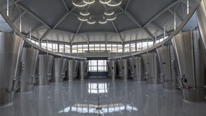 A spacious industrial-style interior with large cylindrical tanks and a high ceiling with circular light fixtures. - Château Tour Saint-Fort (Saint-Estephe)