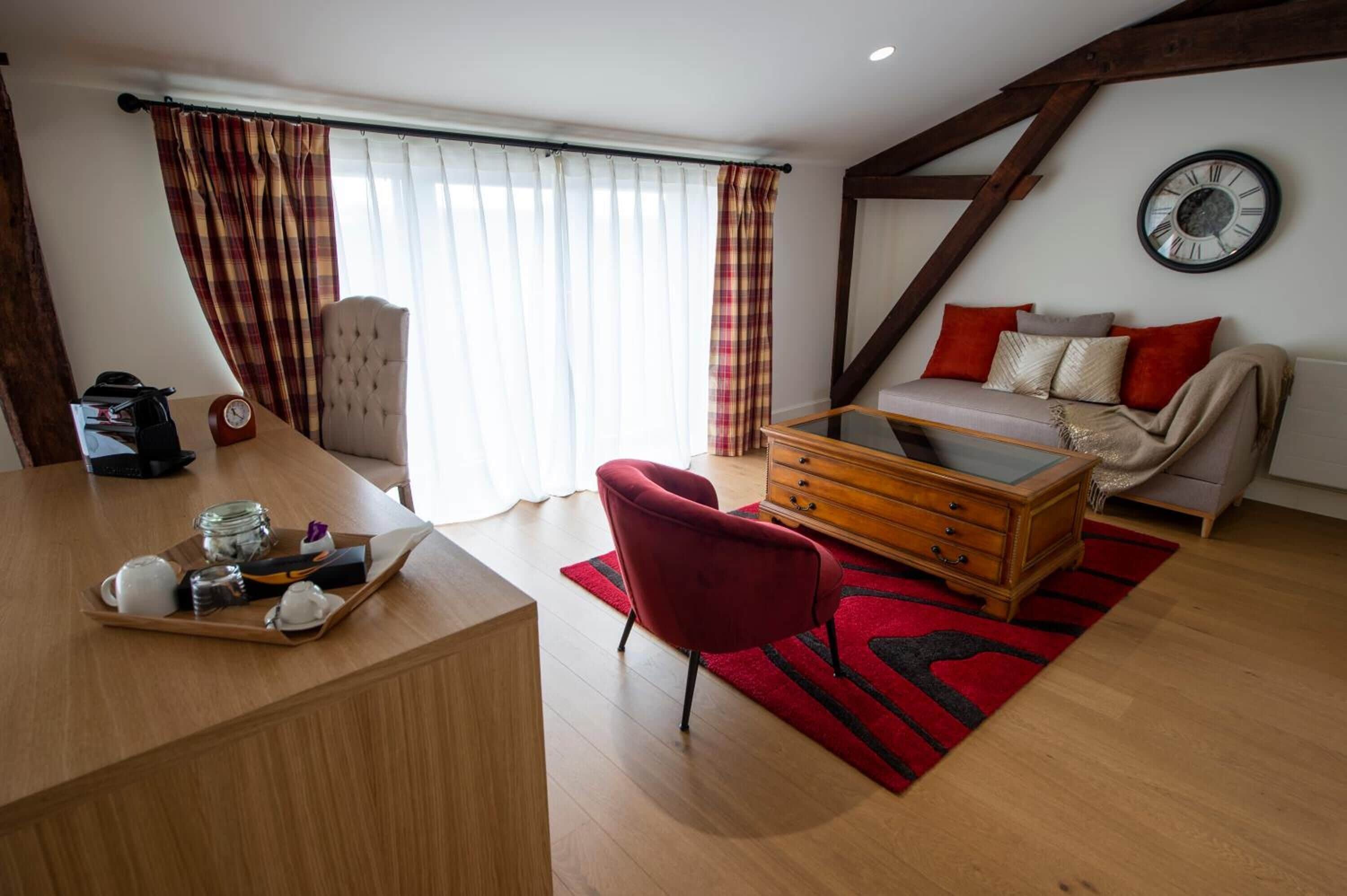 A cozy room with a wooden desk, a red chair, a sofa, and a dining table with a tray of breakfast items.
