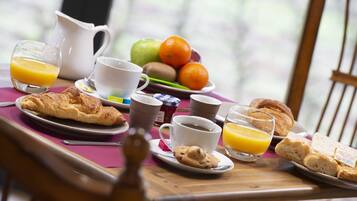 Une table de petit-déjeuner avec des croissants, du jus d’orange, du café et des fruits.