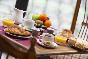 Mesa de café da manhã com croissants, suco de laranja, café e frutas.