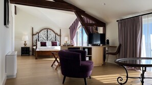 Quarto com cama, escrivaninha, cadeira, televisão e janela com cortinas.