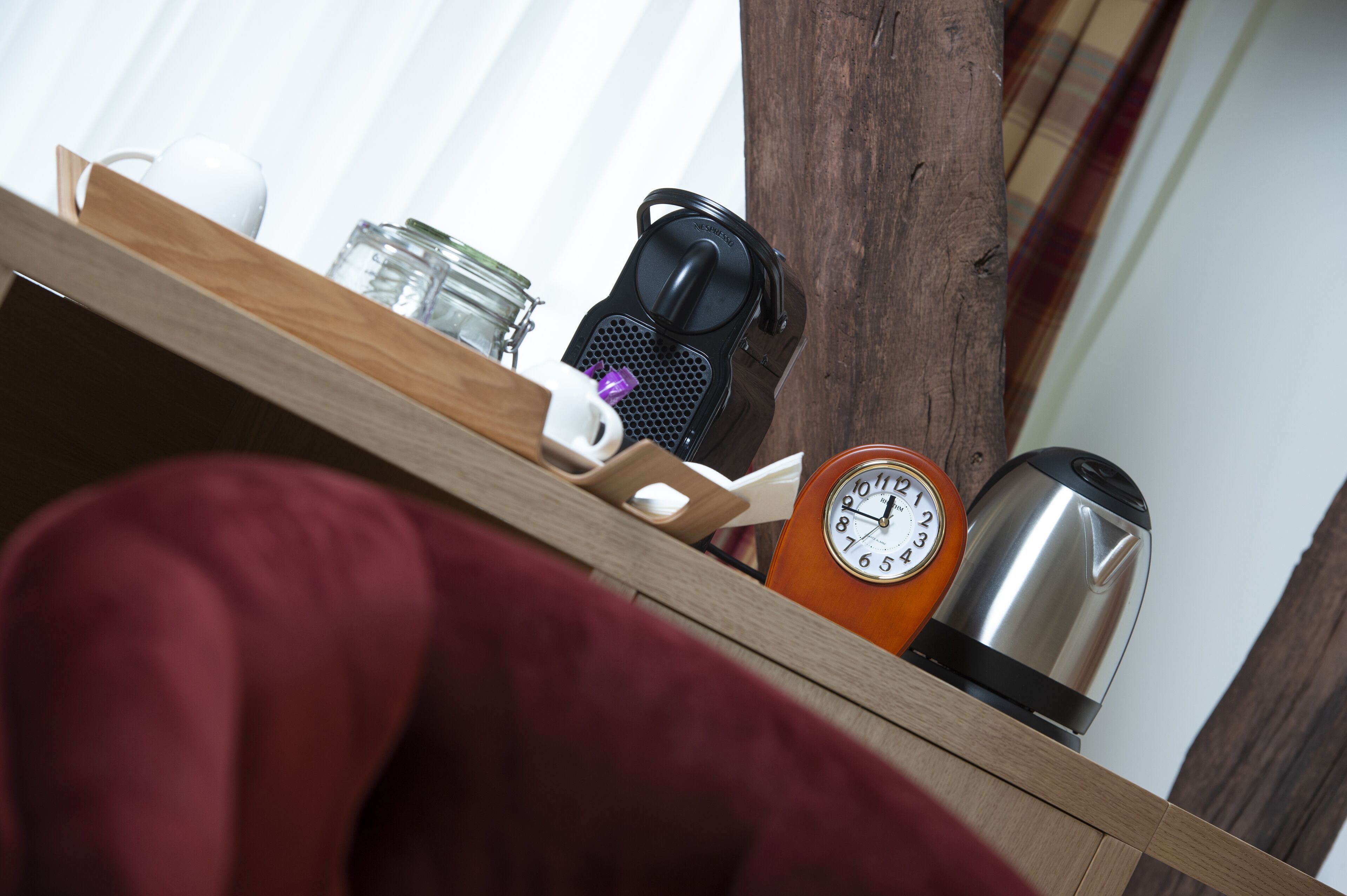 Una estantería de madera con una taza blanca, un tarro de cristal, una cafetera negra, un reloj y un hervidor de acero inoxidable.