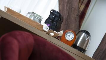 Una estantería de madera con una taza blanca, un tarro de cristal, una cafetera negra, un reloj y un hervidor de acero inoxidable.