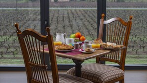 A breakfast table with a view of a vineyard through large windows. - Château Tour Saint-Fort (Saint-Estephe)