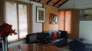 Ein Zimmer mit einem runden Holztisch, einer schwarzen Ledersofa mit roten und grauen Kissen und einem Bild an der Wand.