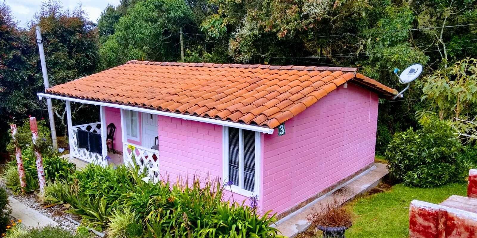 A small pink house with a red-tiled roof, a white porch, and a satellite dish.